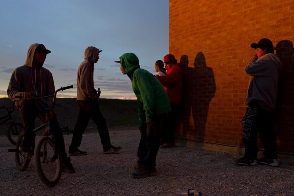 Attawapiskat, Ontario, Canada. Young people gather at dusk outside the Kattawapiskak Elementary School. The suicide crisis that came to light in 2016 was largely impacting youth with the majority of the attempts amongst teenagers. One elder in the community cited a growing disconnect between traditional ways and the younger generation, amplified by the many challenges associated with living in a remote community. "It is important now for young people to understand the colonial policies that have left their communities disconnected" she said. "Only if they can understand what people went through can they articulate why their lives may be in chaos.".
.

Attawapiskat is an isolated First Nation community  located in northern Ontario, Canada, at the mouth of the Attawapiskat River on James Bay. On April 9, 2016, the community of approximately 2000 people declared a state of emergency after being overwhelmed with attempted suicides, over 100 attempts in a ten month period. August 20, 2016. David Maurice Smith/Oculi.